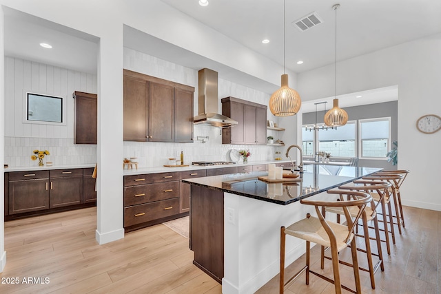 10006 E Rotation Dr, Mesa, AZ 85212 - kitchen with wall chimney exhaust hood, light wood-style floors, backsplash, a kitchen breakfast bar, and recessed lighting