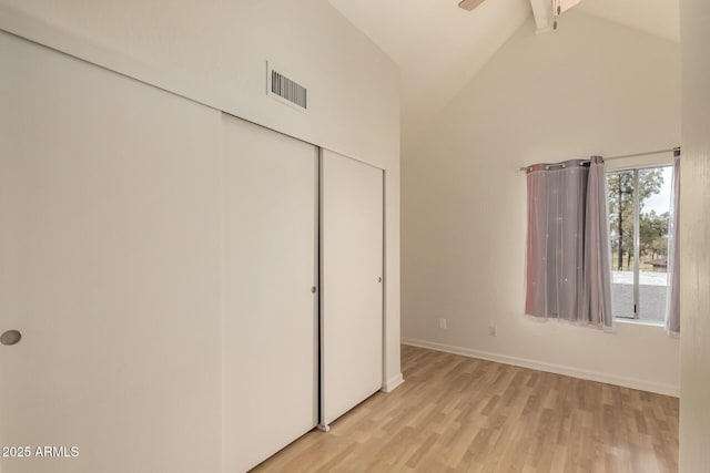 unfurnished bedroom with visible vents, a closet, light wood-style floors, baseboards, and high vaulted ceiling