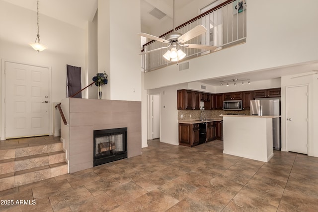 unfurnished living room featuring ceiling fan, visible vents, a towering ceiling, a tile fireplace, and a sink