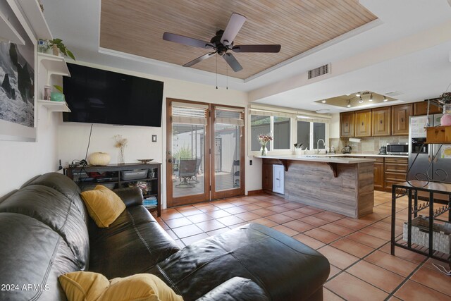 tiled living room with wood ceiling, sink, ceiling fan, and a tray ceiling