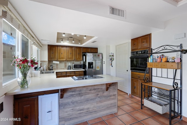 kitchen featuring sink, backsplash, a raised ceiling, black appliances, and kitchen peninsula