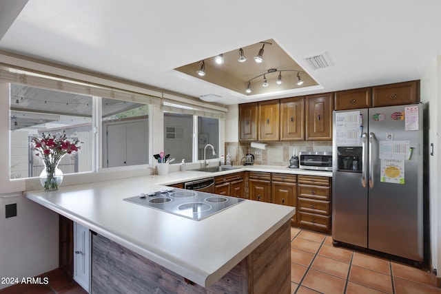 kitchen featuring a tray ceiling, backsplash, kitchen peninsula, appliances with stainless steel finishes, and sink