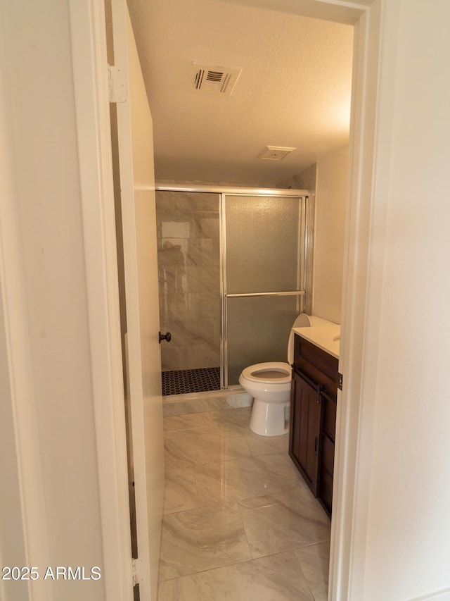 bathroom featuring a shower with door, vanity, and toilet