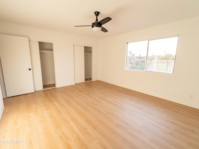 unfurnished bedroom featuring ceiling fan, two closets, and light hardwood / wood-style floors