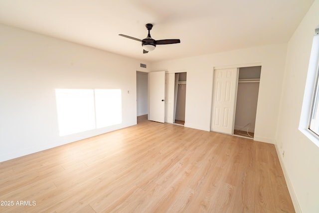 unfurnished bedroom featuring multiple closets, ceiling fan, and light hardwood / wood-style flooring