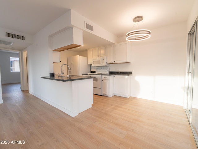 kitchen with white appliances, white cabinetry, hanging light fixtures, kitchen peninsula, and light wood-type flooring