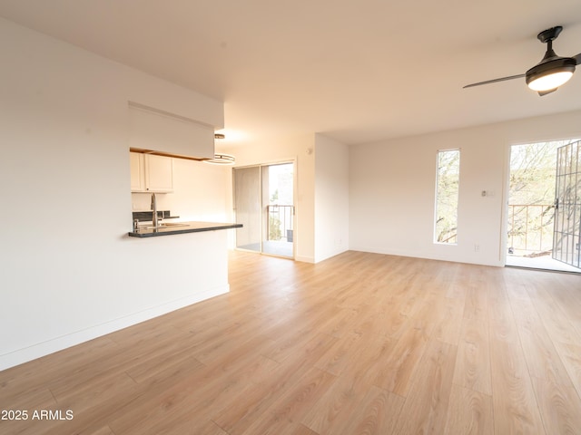 unfurnished living room featuring a healthy amount of sunlight, sink, ceiling fan, and light hardwood / wood-style flooring