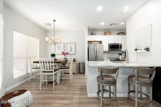 kitchen with stainless steel appliances, light wood-type flooring, light stone counters, hanging light fixtures, and white cabinetry