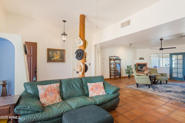 tiled living room with ceiling fan, visible vents, and a glass covered fireplace
