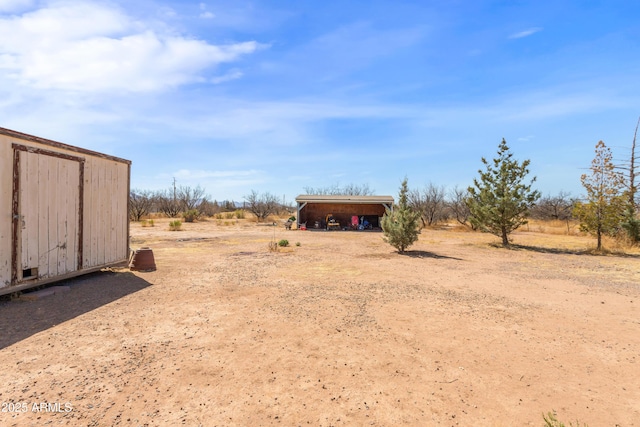 view of yard featuring driveway, a carport, an outdoor structure, and a rural view