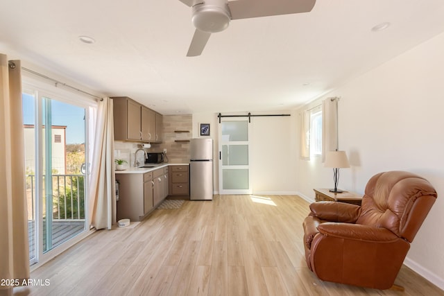 interior space with baseboards, a barn door, light wood finished floors, and ceiling fan