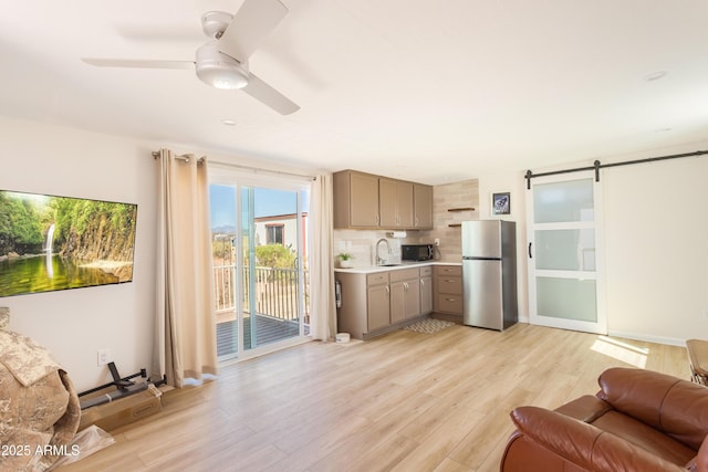 kitchen with gray cabinets, a sink, freestanding refrigerator, black microwave, and light wood-style floors