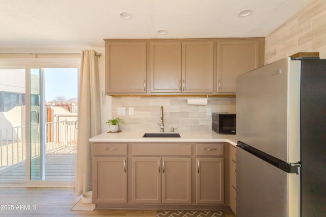 kitchen with decorative backsplash, light countertops, black microwave, a sink, and freestanding refrigerator