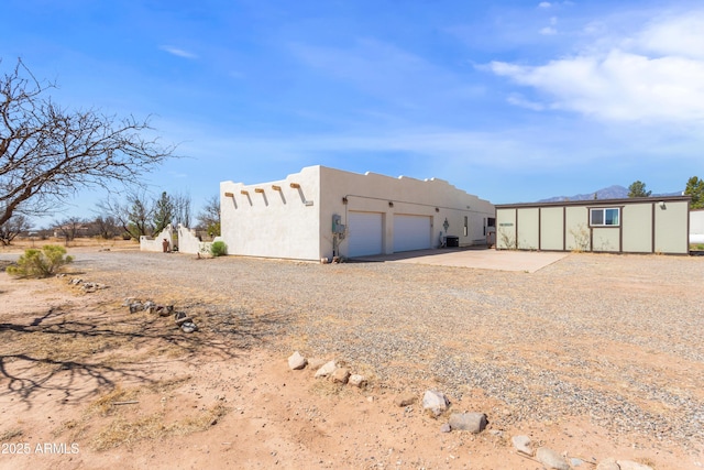 rear view of property featuring stucco siding, an outbuilding, a garage, and concrete driveway