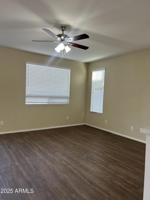 empty room featuring dark wood-type flooring, a ceiling fan, and baseboards