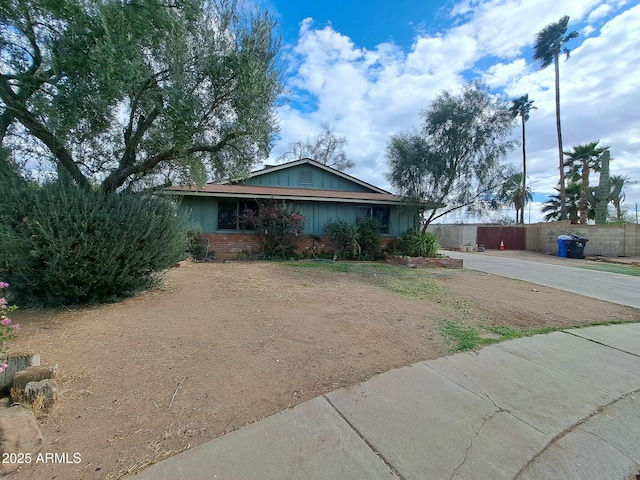 single story home with board and batten siding, brick siding, driveway, and fence