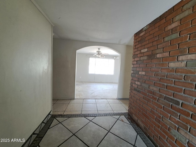 corridor with arched walkways, brick wall, and light tile patterned floors