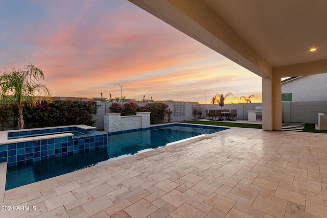 pool at dusk with an in ground hot tub and a patio