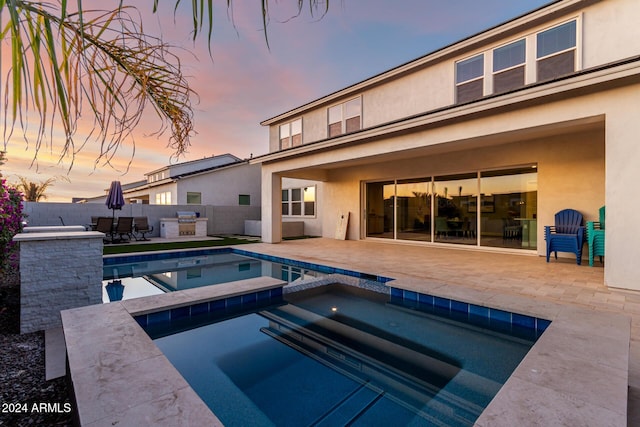 pool at dusk with an outdoor kitchen, a patio area, and an in ground hot tub