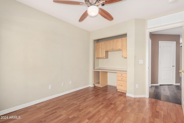 interior space featuring light wood-type flooring, light brown cabinetry, built in desk, and ceiling fan