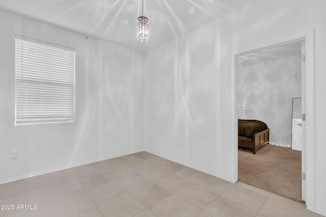 spare room featuring a chandelier, light colored carpet, and light tile patterned flooring