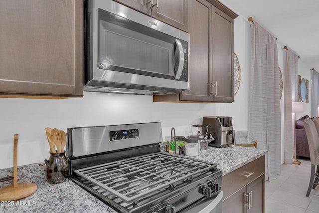 kitchen with light tile patterned floors, light stone countertops, dark brown cabinets, and stainless steel appliances