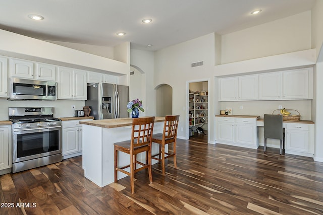 kitchen featuring visible vents, dark wood finished floors, built in desk, appliances with stainless steel finishes, and a kitchen bar