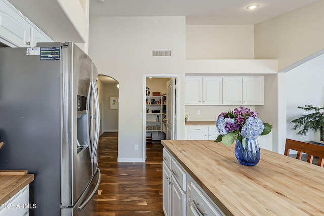 kitchen featuring visible vents, stainless steel fridge, arched walkways, white cabinets, and butcher block counters