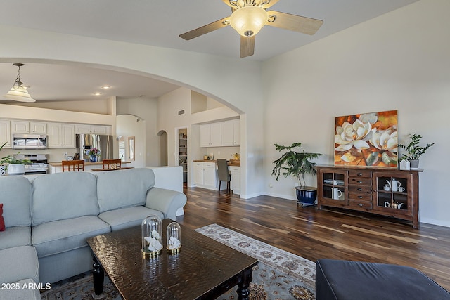 living area with baseboards, arched walkways, dark wood-style floors, high vaulted ceiling, and a ceiling fan