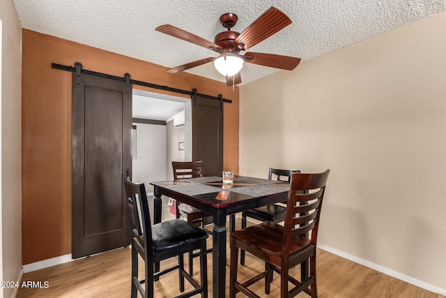 dining area featuring light wood-type flooring, a textured ceiling, a barn door, and ceiling fan