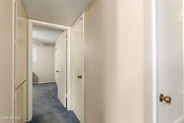 hall featuring dark carpet and a textured ceiling