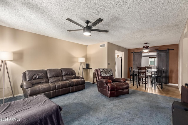 carpeted living room featuring ceiling fan, a barn door, and a textured ceiling