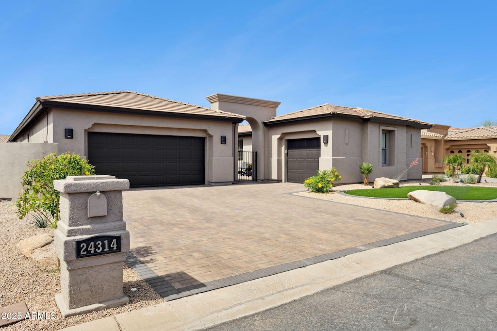 prairie-style home with stucco siding, fence, a tiled roof, decorative driveway, and a garage