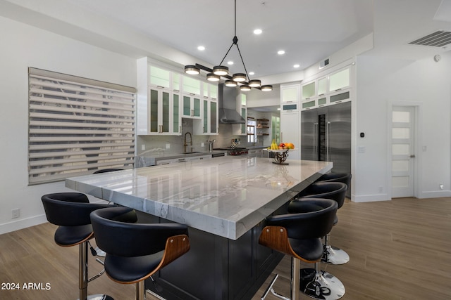 kitchen featuring wall chimney range hood, white cabinets, light wood-style flooring, and decorative backsplash