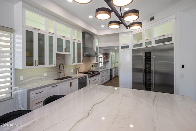 kitchen featuring a sink, white cabinetry, appliances with stainless steel finishes, wall chimney range hood, and visible vents