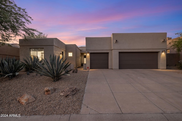 pueblo-style house featuring stucco siding, an attached garage, and concrete driveway
