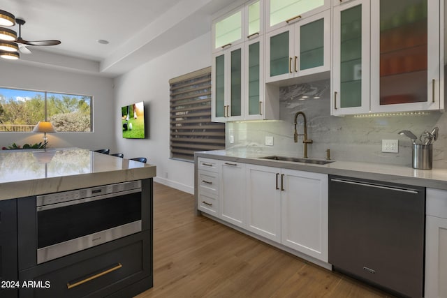 kitchen featuring white cabinets, tasteful backsplash, a sink, light wood-style floors, and stainless steel dishwasher
