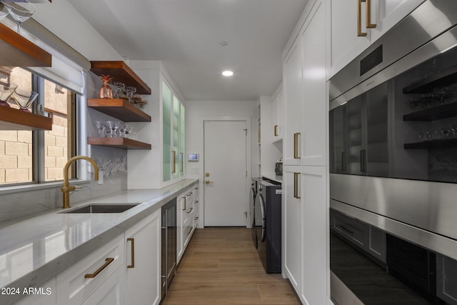 kitchen with washing machine and dryer, a sink, open shelves, light stone countertops, and oven