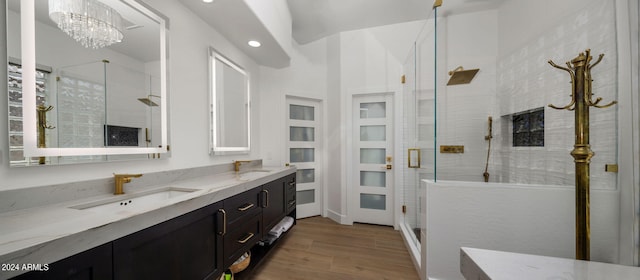 bathroom featuring a notable chandelier, a sink, a shower stall, wood finished floors, and double vanity