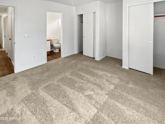 unfurnished bedroom featuring multiple closets, carpet, baseboards, and ensuite bath