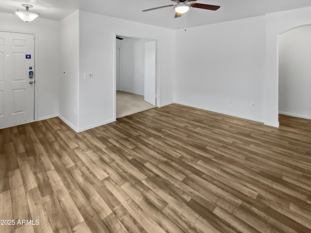 interior space featuring arched walkways, ceiling fan, baseboards, and wood finished floors