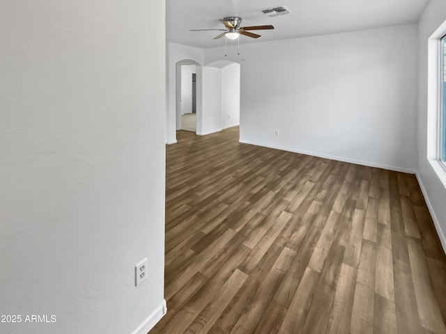 unfurnished room featuring arched walkways, visible vents, dark wood-type flooring, ceiling fan, and plenty of natural light