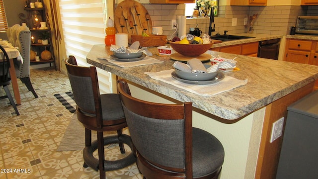 kitchen featuring backsplash, sink, a kitchen bar, and black dishwasher