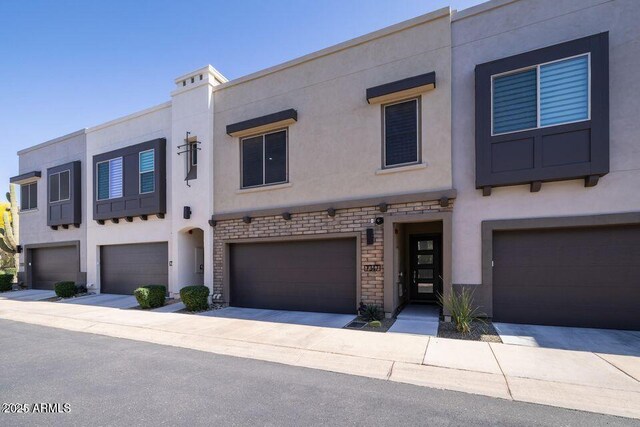 townhome / multi-family property with stucco siding, stone siding, and a garage