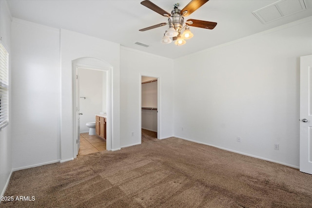 unfurnished bedroom featuring a walk in closet, ensuite bathroom, light carpet, and visible vents