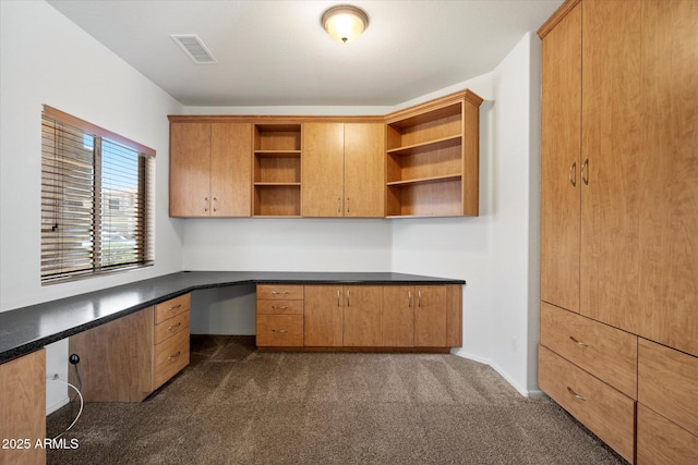 unfurnished office featuring baseboards, dark colored carpet, built in desk, and visible vents