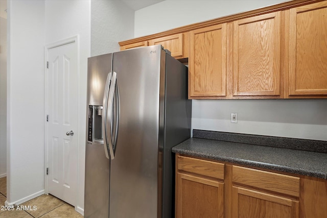 kitchen featuring brown cabinets, stainless steel refrigerator with ice dispenser, dark countertops, and light tile patterned flooring