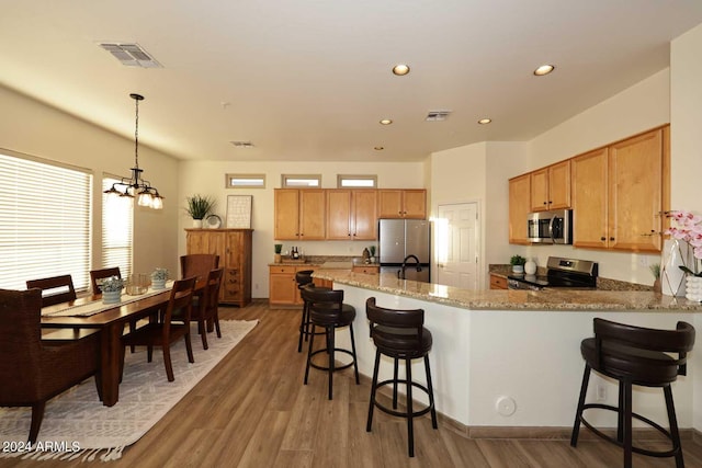 kitchen featuring dark hardwood / wood-style flooring, light stone counters, stainless steel appliances, hanging light fixtures, and a breakfast bar area