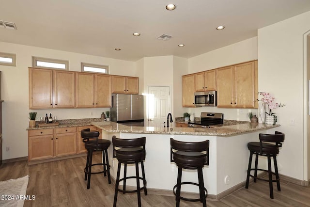 kitchen featuring kitchen peninsula, appliances with stainless steel finishes, light stone countertops, a breakfast bar, and dark hardwood / wood-style floors