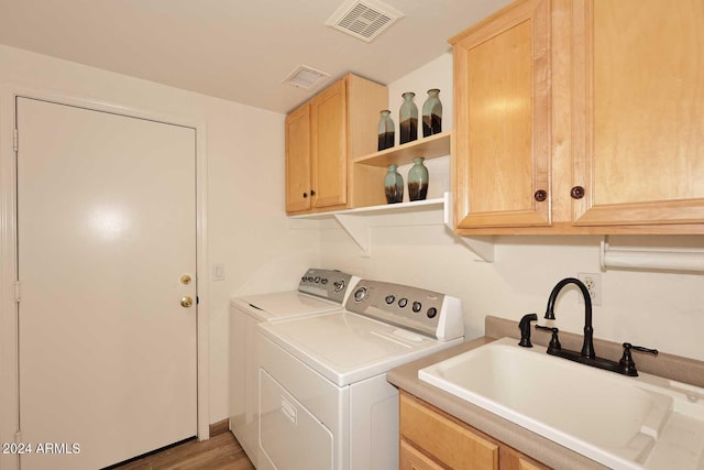 clothes washing area featuring washing machine and dryer, sink, cabinets, and light hardwood / wood-style flooring